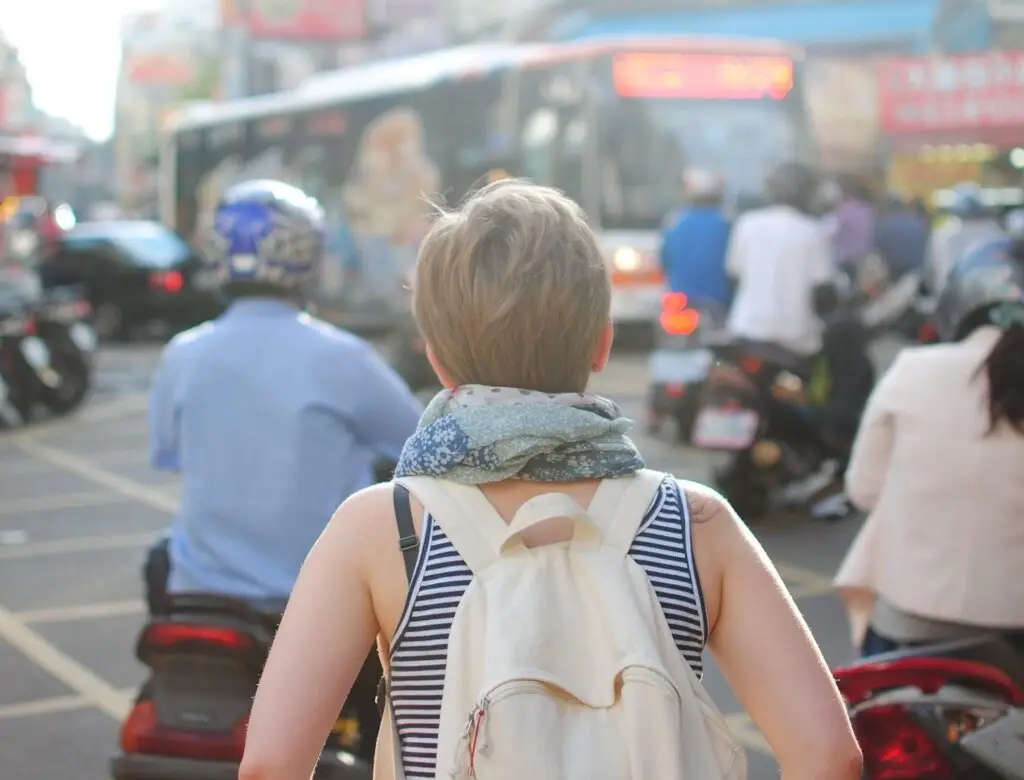 A woman surrounded by mo-peds walks through a crowded city scene.