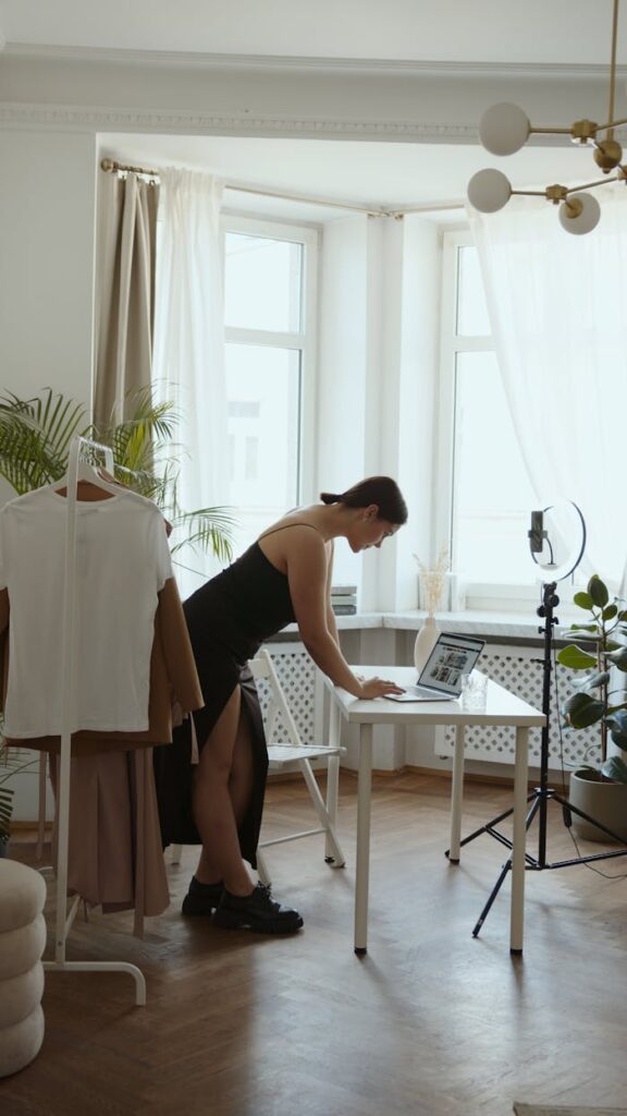 A woman working in a home office with camera set up, leaning over a laptop
