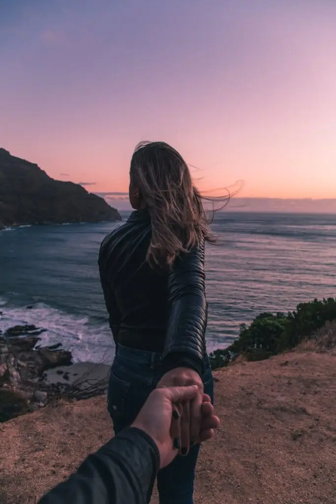 Couple holding hands by the ocean with a stunning sunset view in Cape Town.