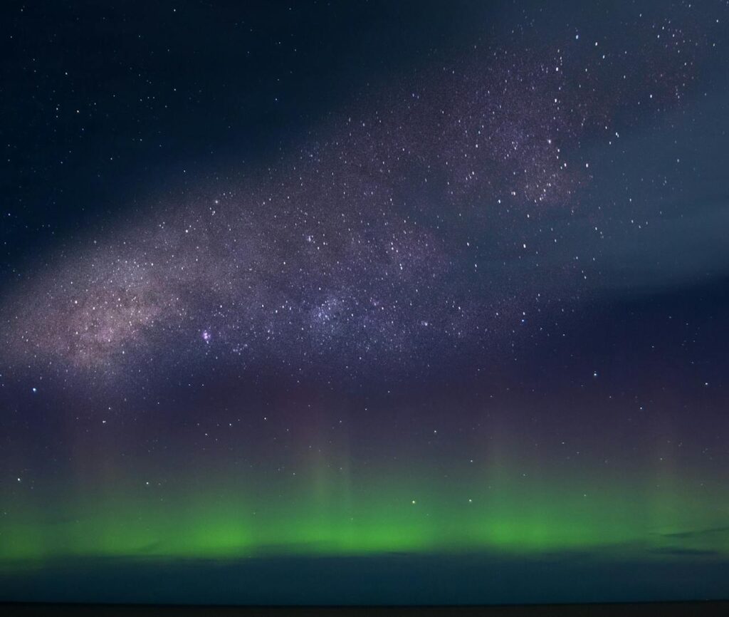 Marvel at the breathtaking view of the aurora borealis under the Milky Way in a starry night sky.