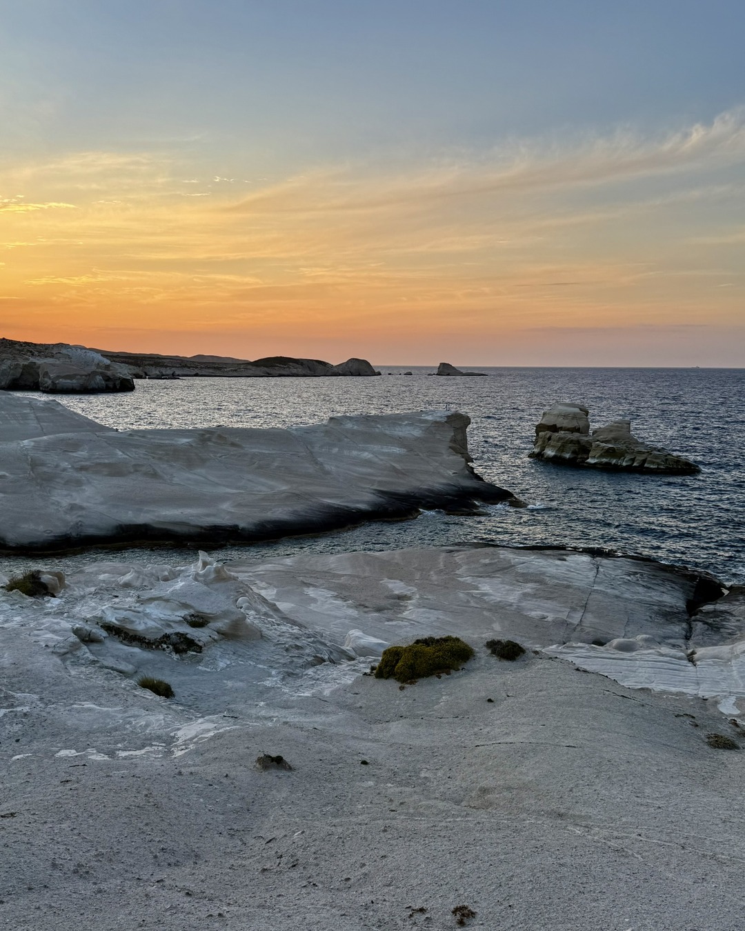 Warm late-day light falls across white rock formations and the sea at Sarakiniko on the Greek island of Milos.